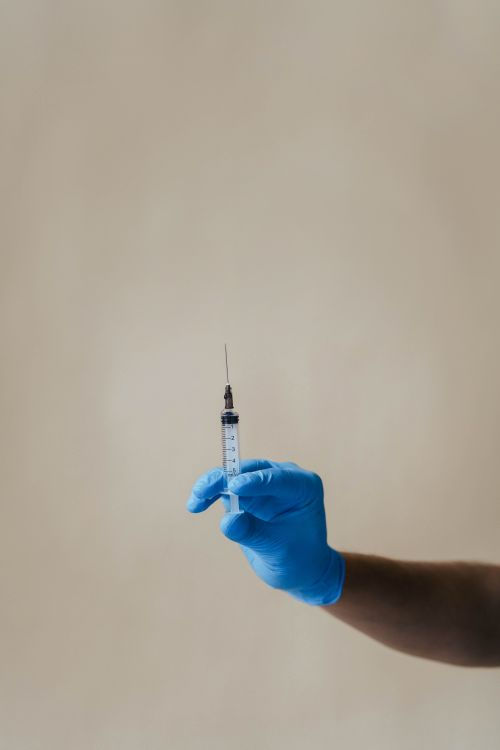 A healthcare worker in blue gloves holding a clinical syringe, representing vaccine administration in a trial setting.