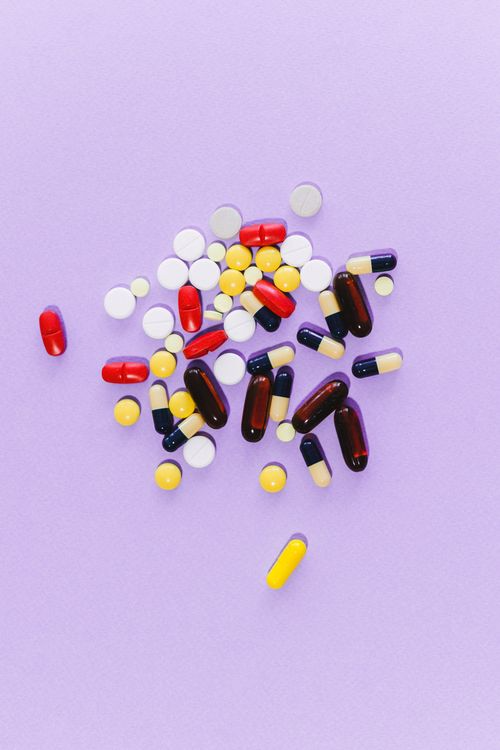 Assorted pharmaceutical pills and capsules on a lavender background, representing conventional vaccine and drug development.