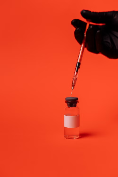 A vaccine vial and syringe on an orange background, representing clinical trial administration.
